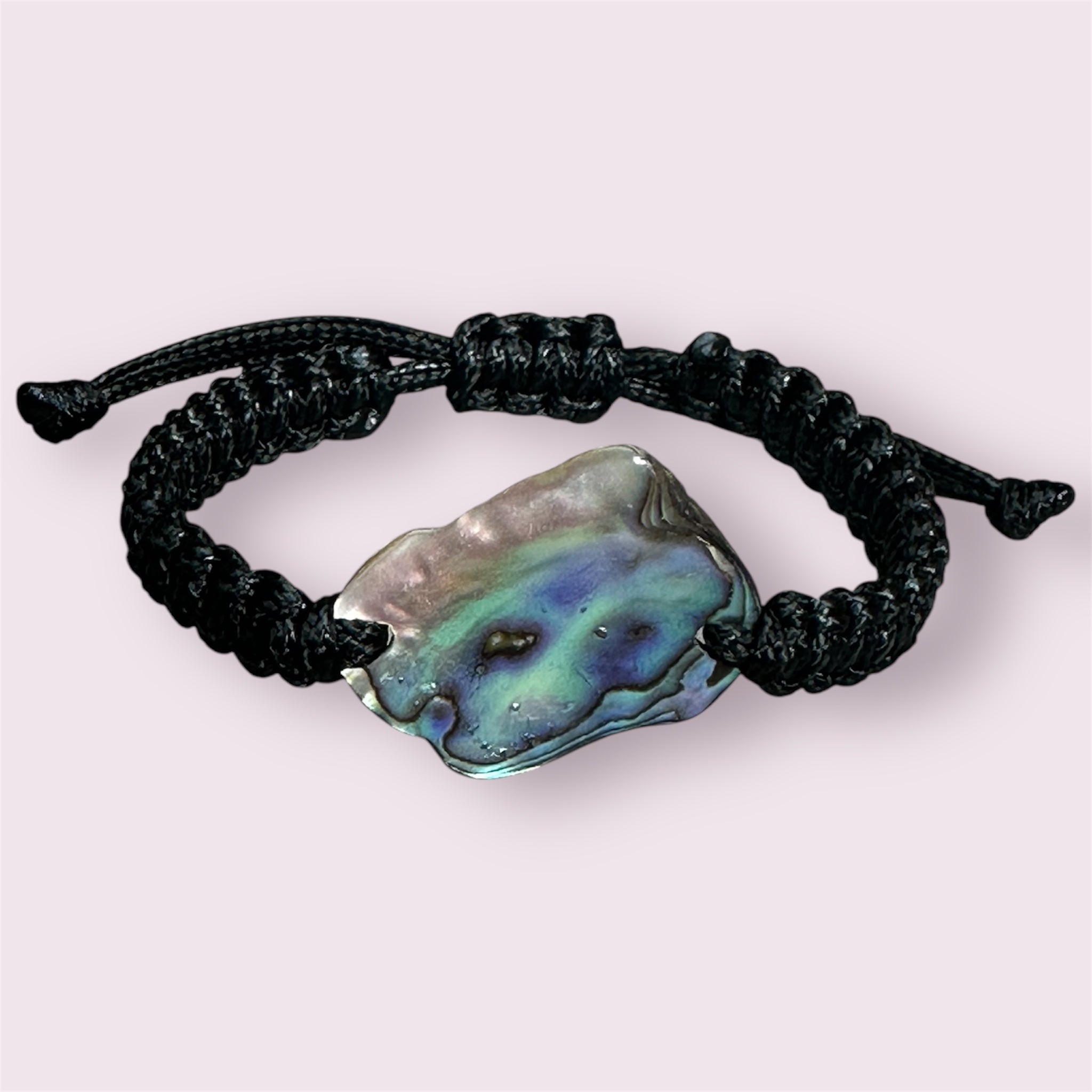 Black polyester knotted bracelet with vibrant NZ Paua shell, photographed on a stone background.