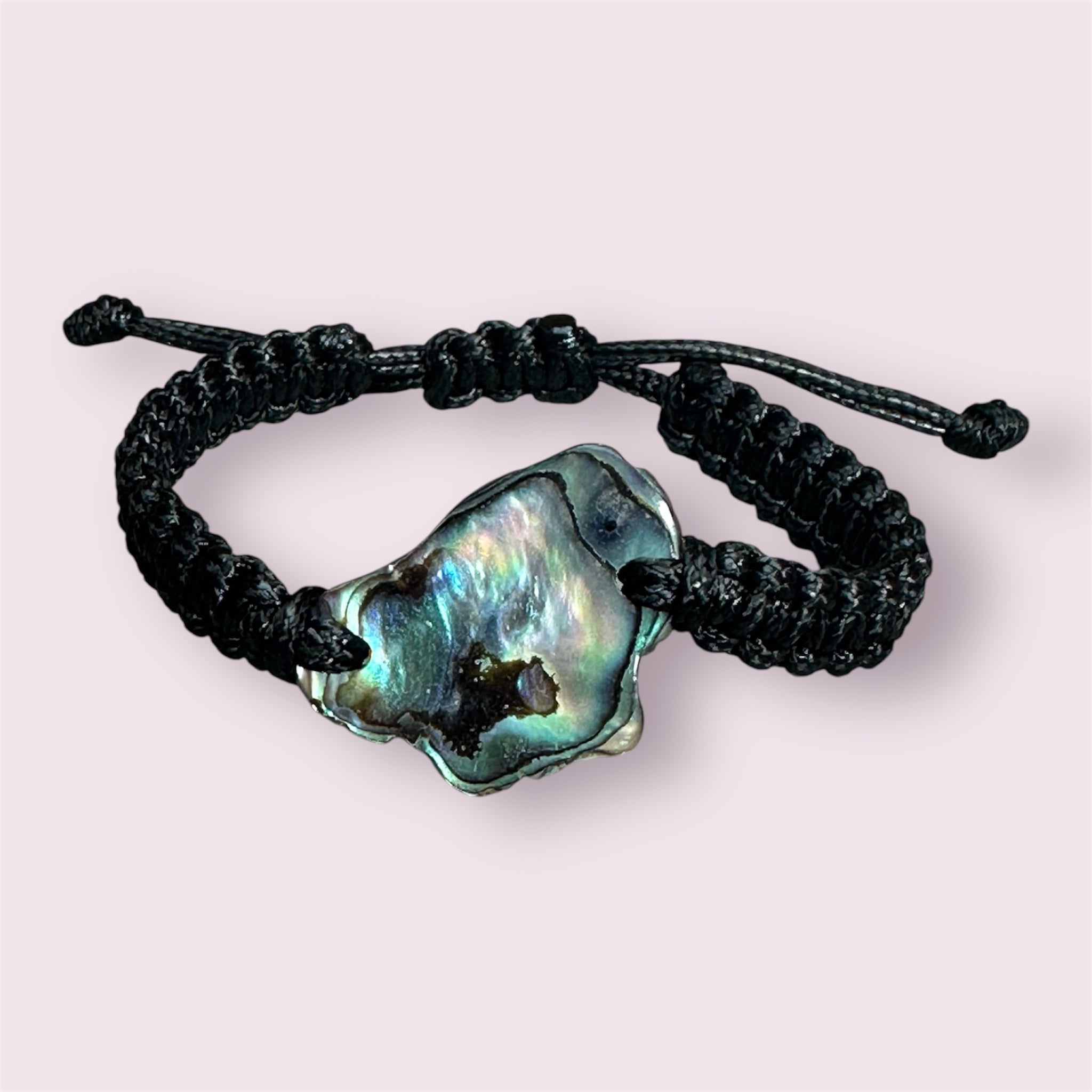 Paua shell bracelet with square black knots, laid flat to highlight the natural iridescence.