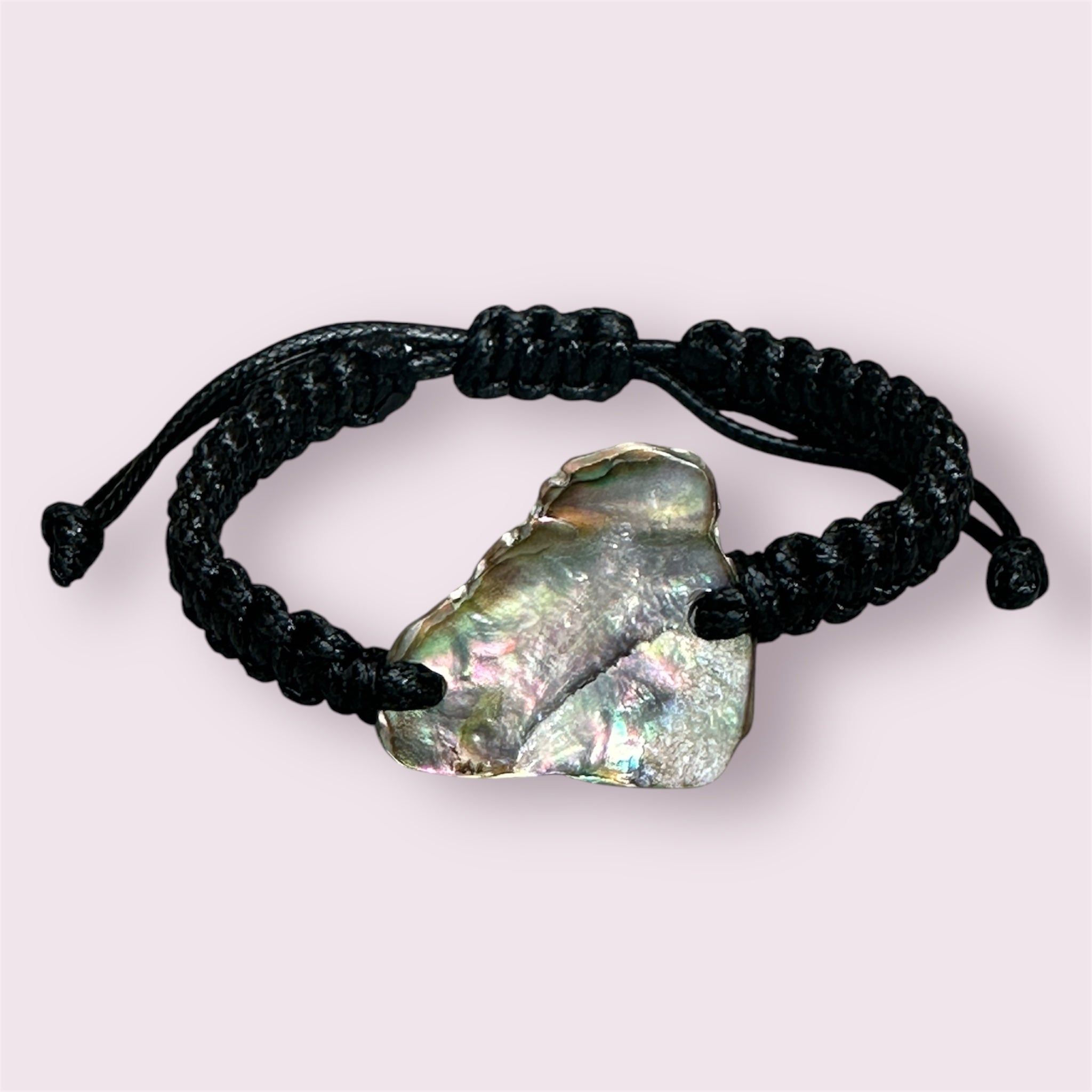 Detail shot of Paua shell set in black knotted cord, with focus on the shell’s natural colour variations.