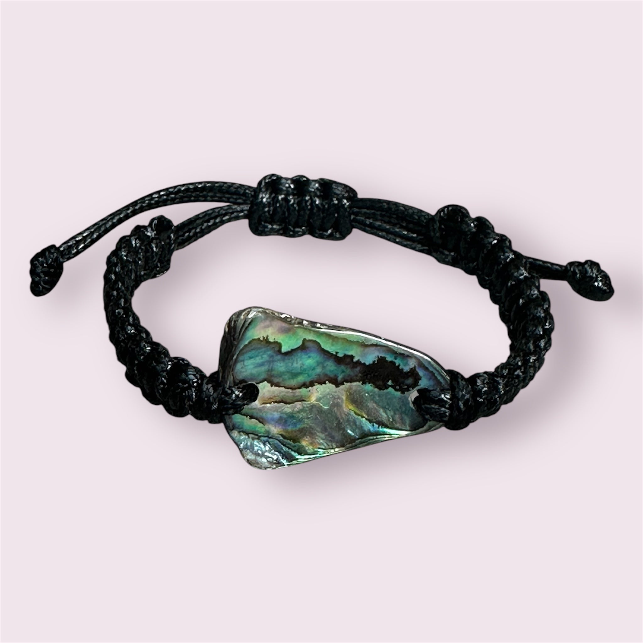 Black knotted bracelet with shimmering shell, styled next to shells and beach elements.