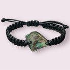 Black string bracelet showcasing a shimmering Paua shell, styled flat on a neutral surface.